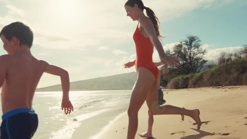 Slow motion shot of a happy mother and her two young sons running together on a beautiful sunny beach