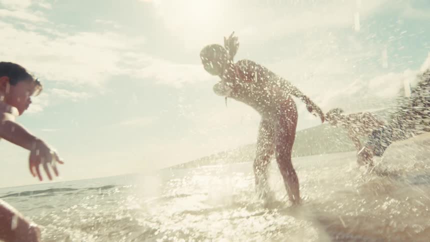 Carefree children joyfully run and splash in the shallow ocean water on a sunny day in slow motion