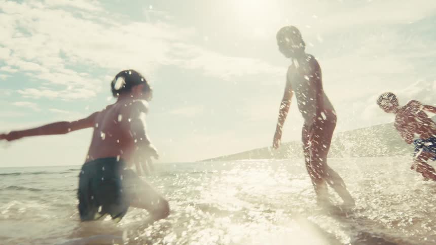 Carefree children joyfully run and splash in the shallow ocean water on a sunny day in slow motion