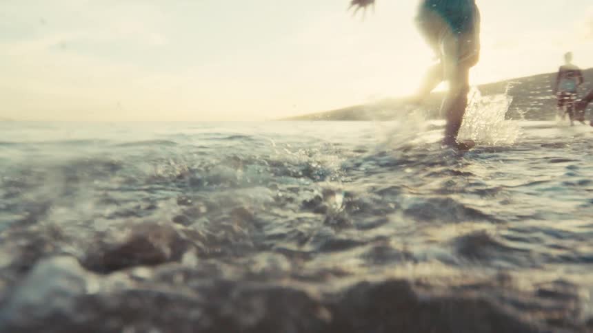 Slow motion shot of a young boy running and splashing in the shallow ocean water along the beach during a beautiful sunset