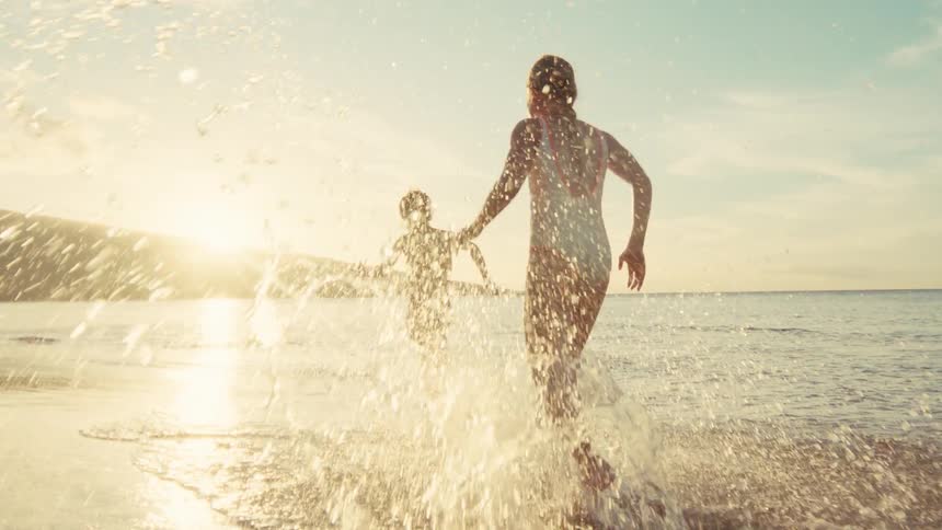 Two children run and splash through the shallow ocean water at sunset in a beautiful slow motion cinematic shot
