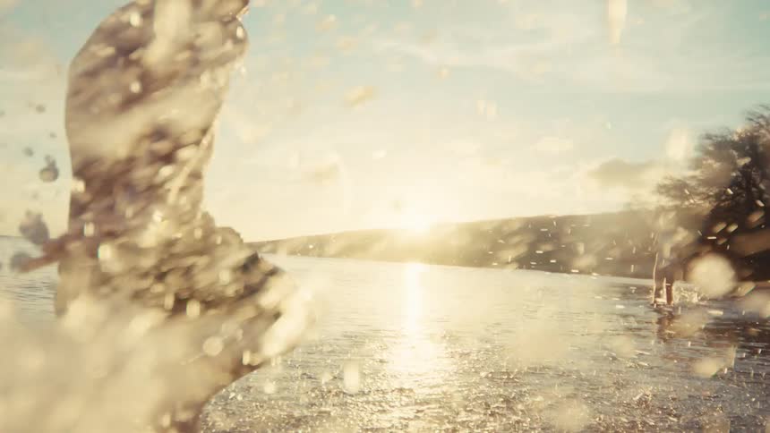 A joyful young boy splashes through the shallow ocean water as the sun sets in a beautiful, warm glow