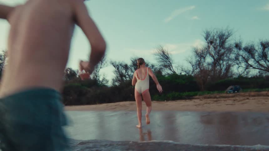 A joyful family with a young boy and girl splash each other in the ocean as they run towards the beach at sunset in slow motion
