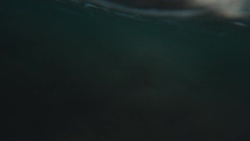 Immersive point-of-view of being caught in an ocean wave, from the initial crash to being submerged and resurfacing to a calm sea at dusk