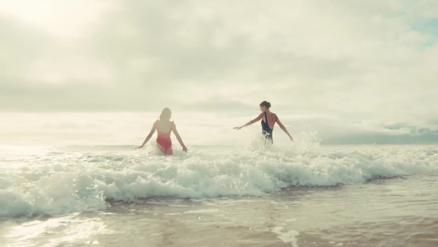 Two carefree women in swimsuits joyfully play and splash in the ocean waves in slow motion