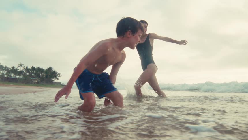 A mother and son share a joyful moment, splashing and playing in the shallow ocean waves in beautiful slow motion