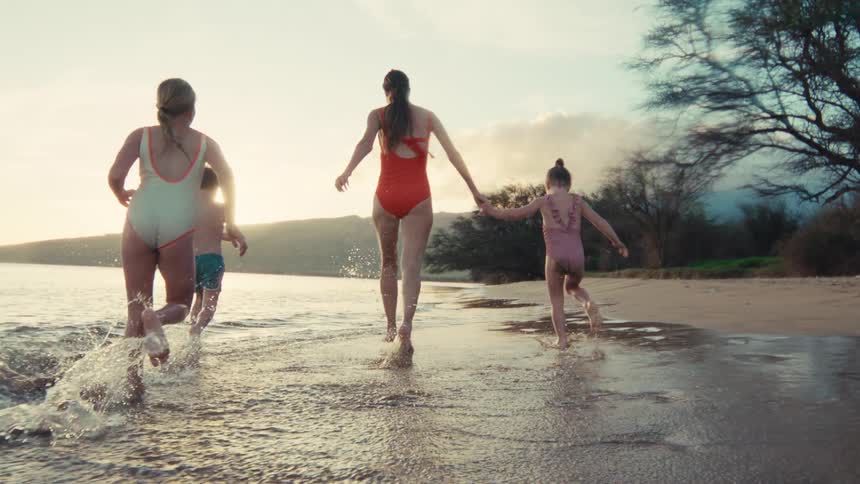 Slow motion shot of a happy family running and splashing along the ocean shoreline at sunset