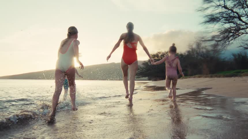 Slow motion shot of a happy family running and splashing along the ocean shoreline at sunset