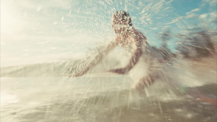 A young girl playfully runs towards the camera in the shallow ocean waves, splashing and diving into the water in slow motion on a beautiful day