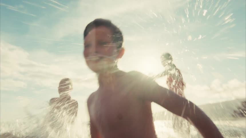 Dreamy slow-motion footage captures joyful kids splashing water at the camera while playing in the ocean on a sunny day
