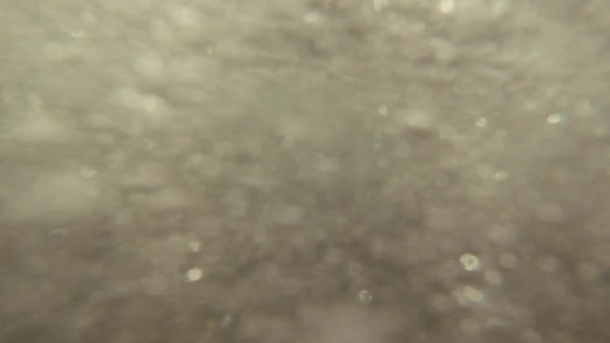 An abstract, out-of-focus underwater shot captures turbulent water and floating bubbles in slow motion