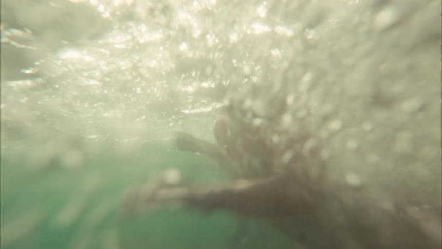 A joyful young girl in a swimsuit playfully splashes water before diving into the ocean in slow motion