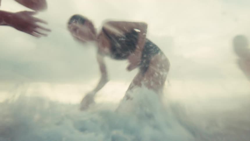 A joyful mother and her two children playfully splash each other in the ocean waves in an immersive, slow-motion shot