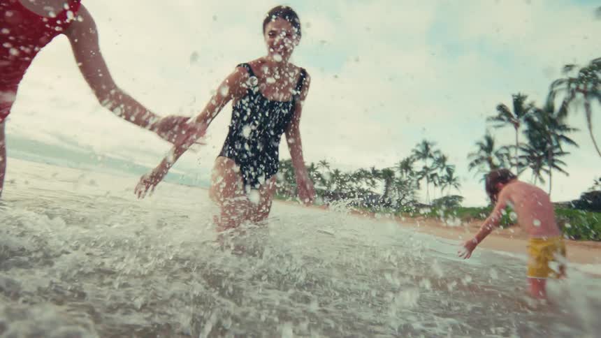 A joyful mother and her children laugh as they splash each other in the shallow ocean waves in slow motion