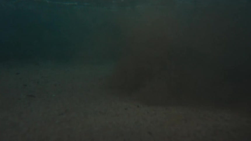 An immersive view from the ocean's surface slowly submerging into the murky, sandy water below