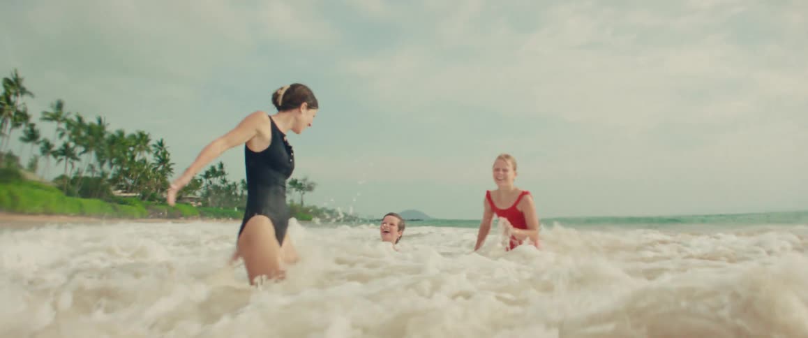 A large ocean wave crashes over a mother and her two children in slow motion as they play together at the beach