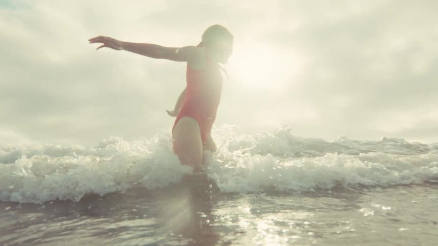 A young girl and her mother joyfully play in the ocean as a wave splashes over the camera in slow motion