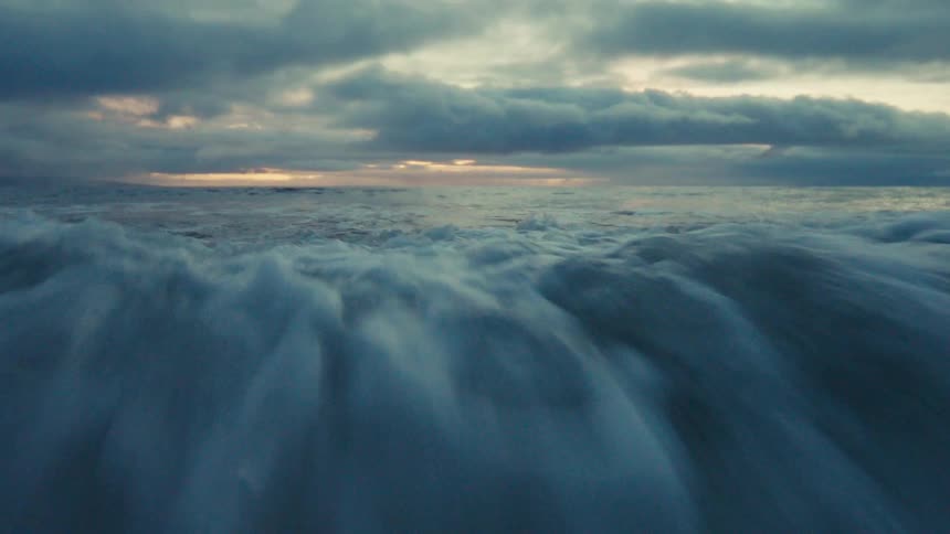 Intense slow-motion view from inside the water as powerful ocean waves crash over the camera under a stormy sky at dusk
