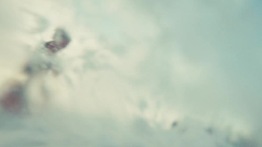 A young boy kneels in the shallow ocean surf as a wave crashes over him and the camera in slow motion