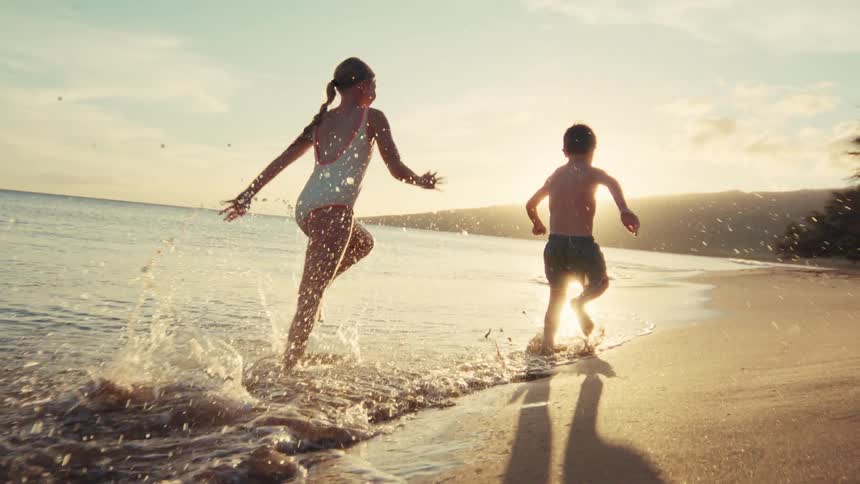Carefree siblings joyfully run along the shoreline, splashing in the waves during a magical golden sunset