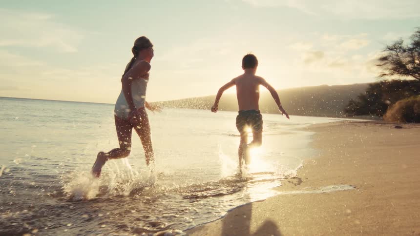 Carefree siblings joyfully run along the shoreline, splashing in the waves during a magical golden sunset