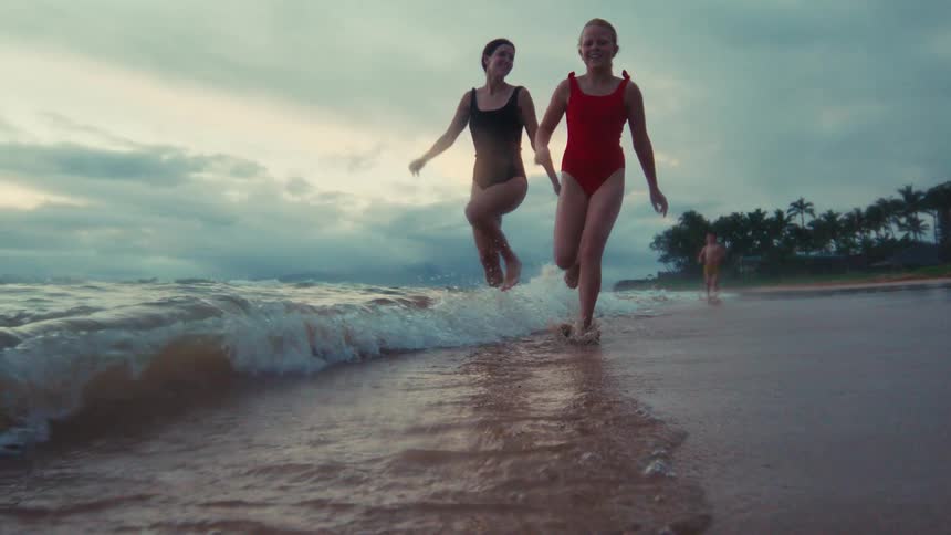 Two young girls run and splash through the shallow waves on a tropical beach in super slow motion