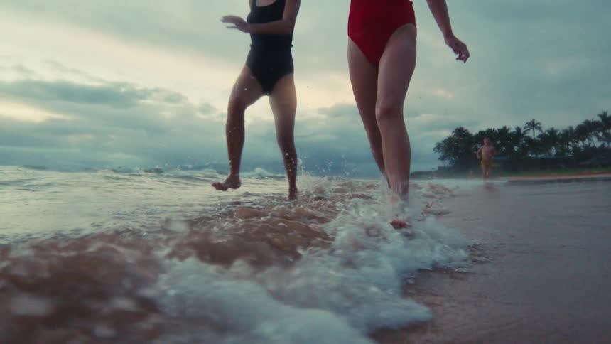 Two young girls run and splash through the shallow waves on a tropical beach in super slow motion