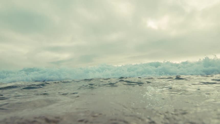 A dramatic slow-motion shot from the water's surface as a powerful ocean wave crests and crashes towards the camera