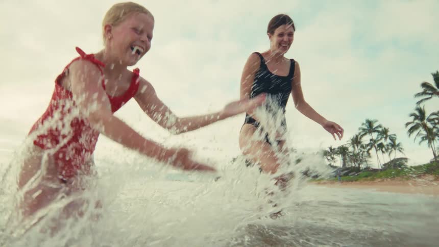 A joyful mother and her children laugh while splashing and playing together in the shallow ocean waves in slow motion