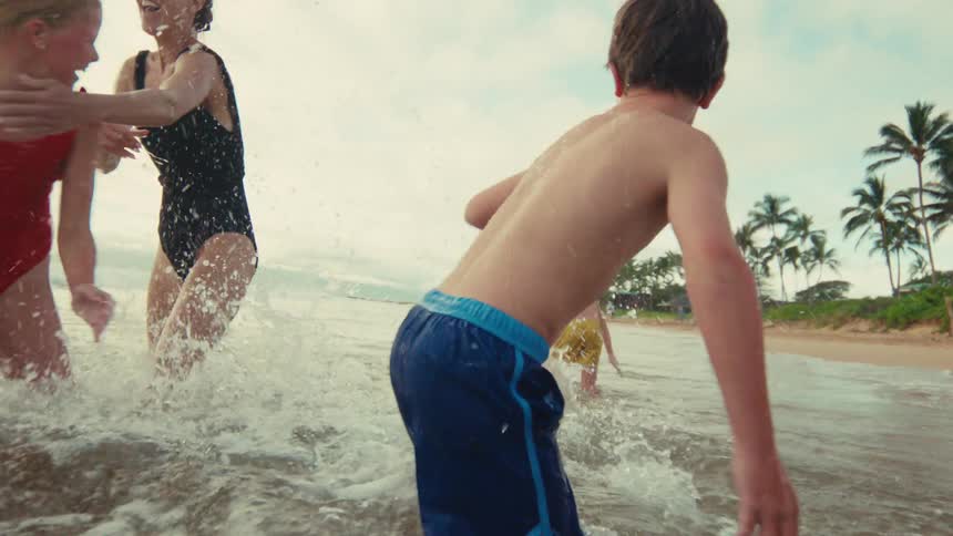 A joyful mother and her children laugh while splashing and playing together in the shallow ocean waves in slow motion