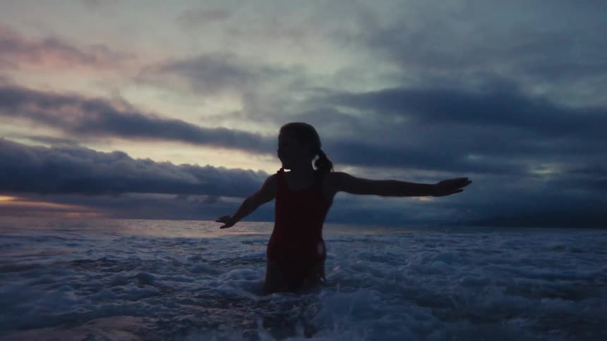 A young girl in a red swimsuit joyfully plays in the crashing ocean waves at sunset in slow motion