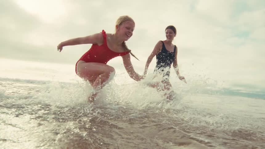 A joyful young girl and her mother laugh and splash in the shallow ocean waves during their tropical beach vacation