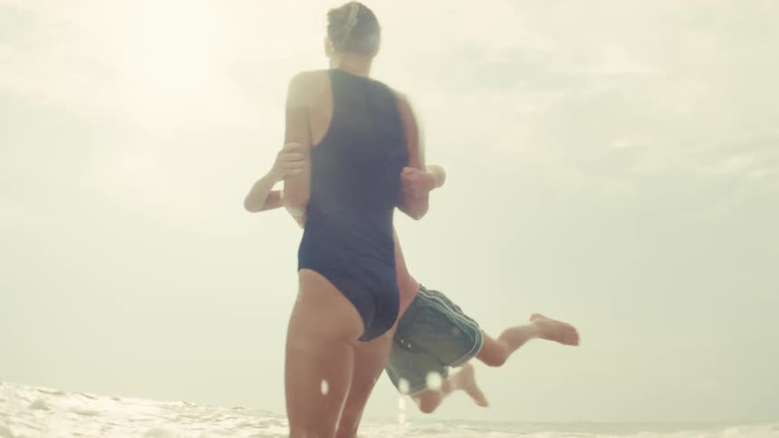 A loving mother playfully spins her young son around in the gentle ocean waves as the bright sun shines down