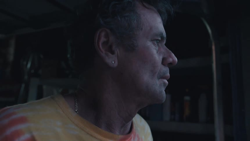 A close-up profile shot of a concerned older man looking off-camera in a dimly lit room