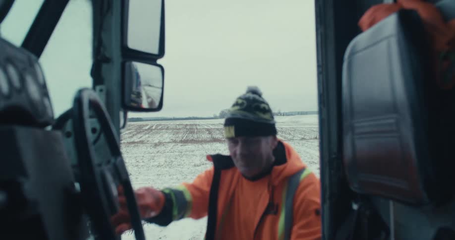 Slow motion shot of a male driver in an orange jacket getting into the cab of his truck on a cold winter day