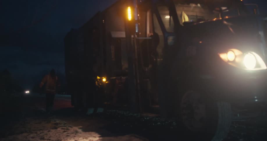 A garbage collector walks to their truck in slow motion during the dark, cold pre-dawn hours
