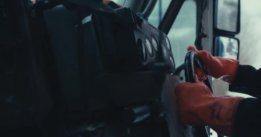 A close-up shot of a driver's hands in orange gloves steering a large truck through a snowy landscape during winter