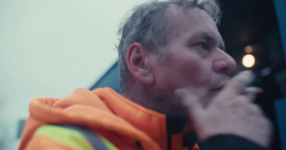 A manual laborer thoughtfully smokes a cigarette in slow motion on a cold day