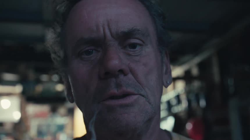 An intense, moody close-up of a weathered older man taking a long drag from his cigarette in a dark room