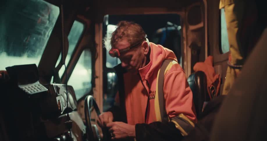 A weary sanitation worker wearing a headlamp gets into his truck to start his cold night shift