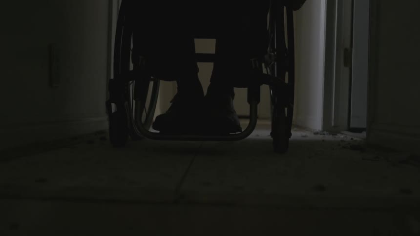 A man wheels his chair down a dark hall