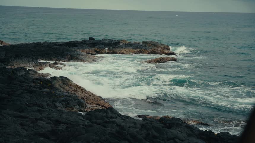 Slow motion shot of powerful ocean waves crashing against a dramatic, rocky volcanic coastline