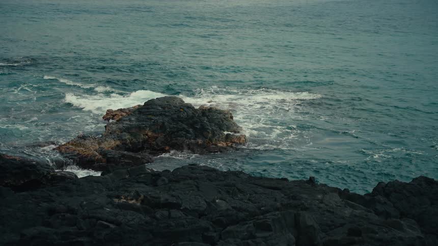 Gentle ocean waves wash over dark volcanic rocks on a tranquil coastline