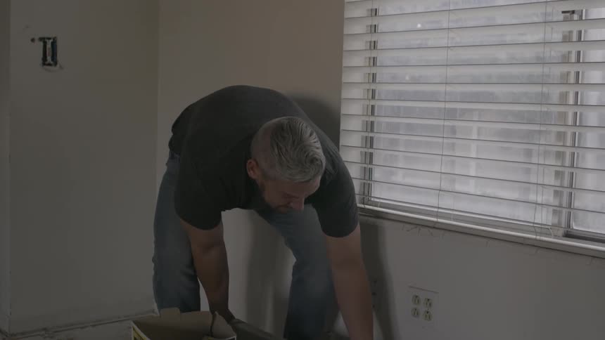 A man is setting a roll of foam down in a living area