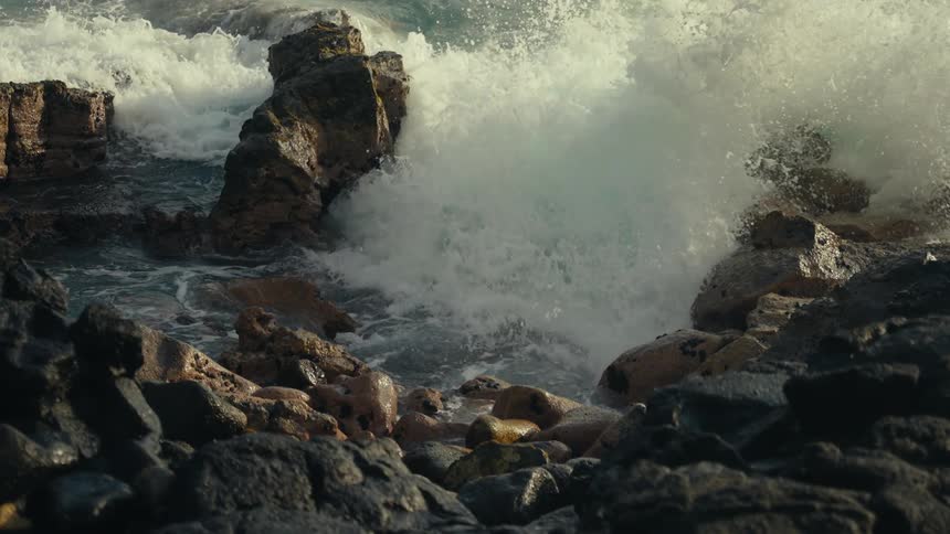 Powerful turquoise ocean waves crash against a rocky shore in dramatic slow motion