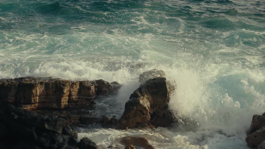 A powerful ocean wave crashes against a rocky shoreline in dramatic slow motion