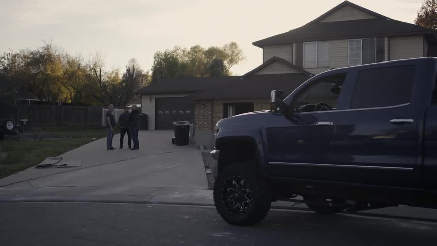 A pickup truck pulls up outside a house where three men are standing