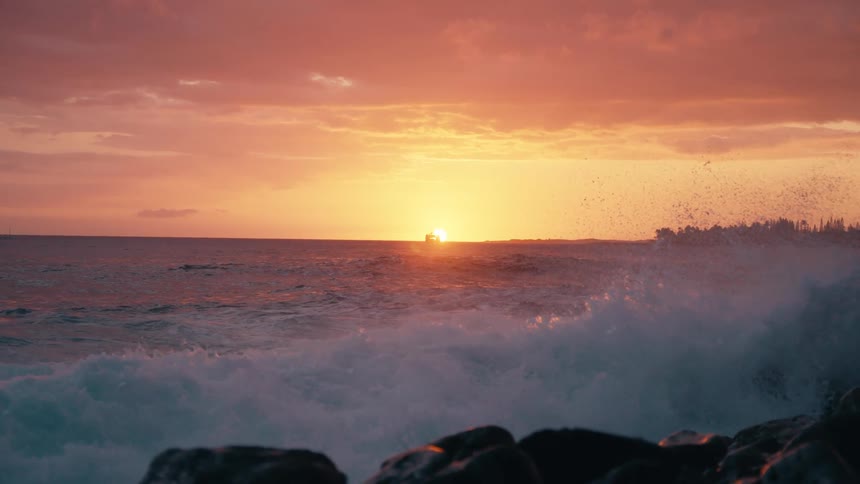 A powerful ocean wave crashes against a rocky shoreline in stunning slow motion during a vibrant sunset