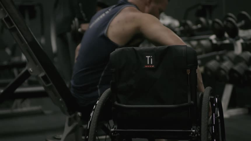 Man moving himself from a workbench into a wheelchair in a gym