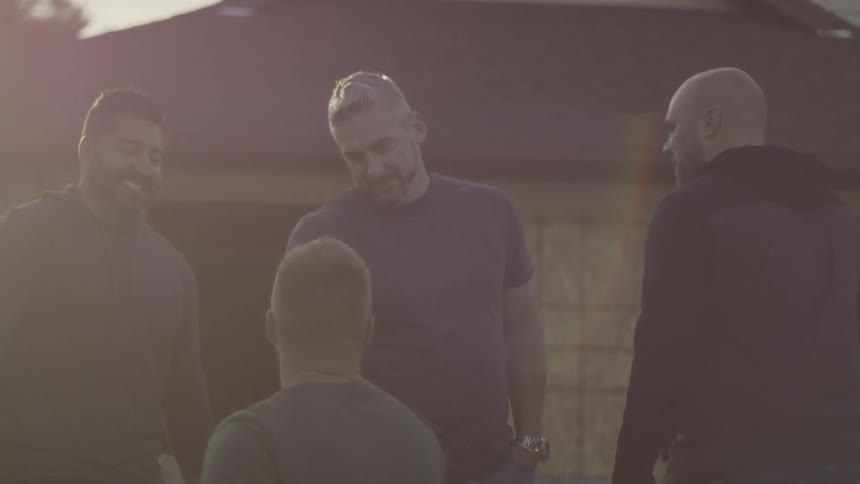 Group of men stand in a driveway talking at sunset